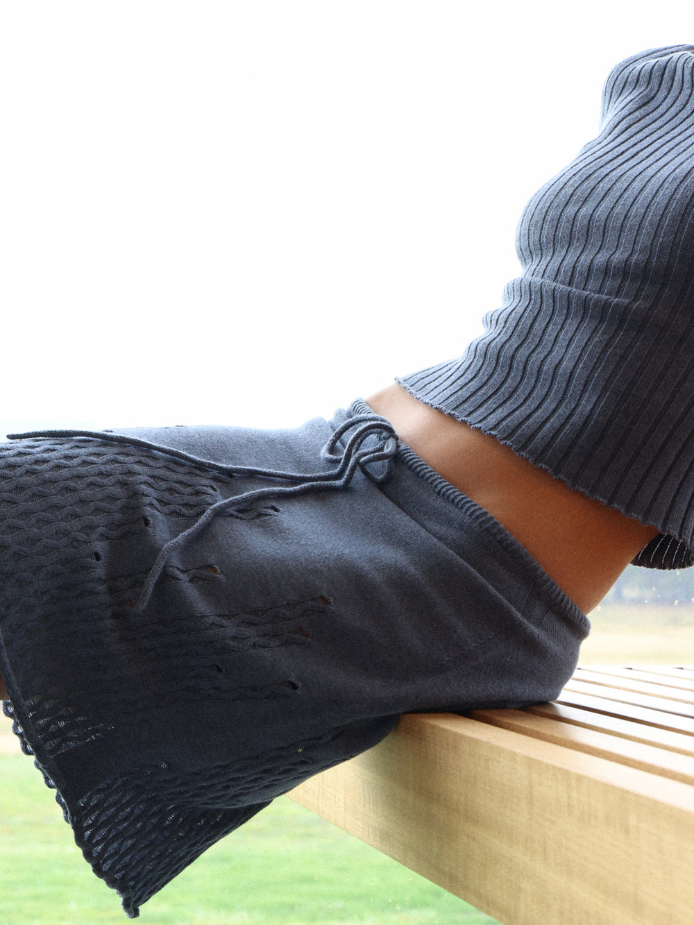 Close up image of reclined model wearing Fruitchouli knitted skirt and ribbed mock neck in denim cotton cashmere. 
